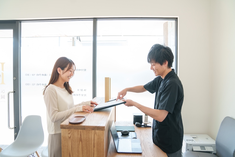 受付カウンターで書類を渡す施術者と来院者