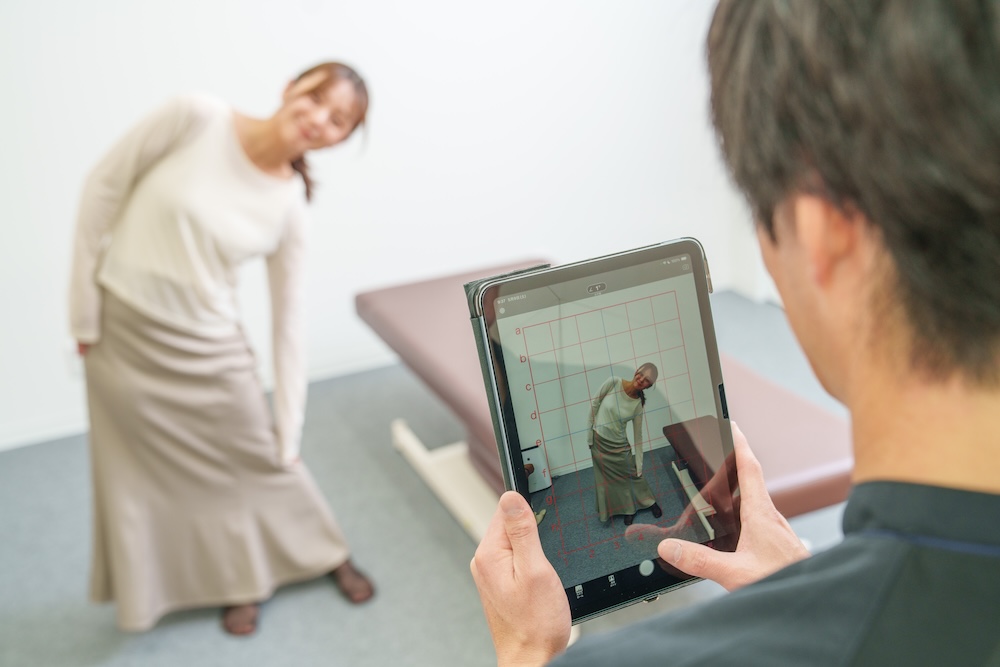 仰向けの患者の脚を動かして確認する施術者