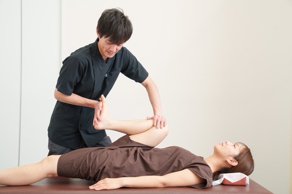 仰向けの患者の脚を動かして確認する施術者