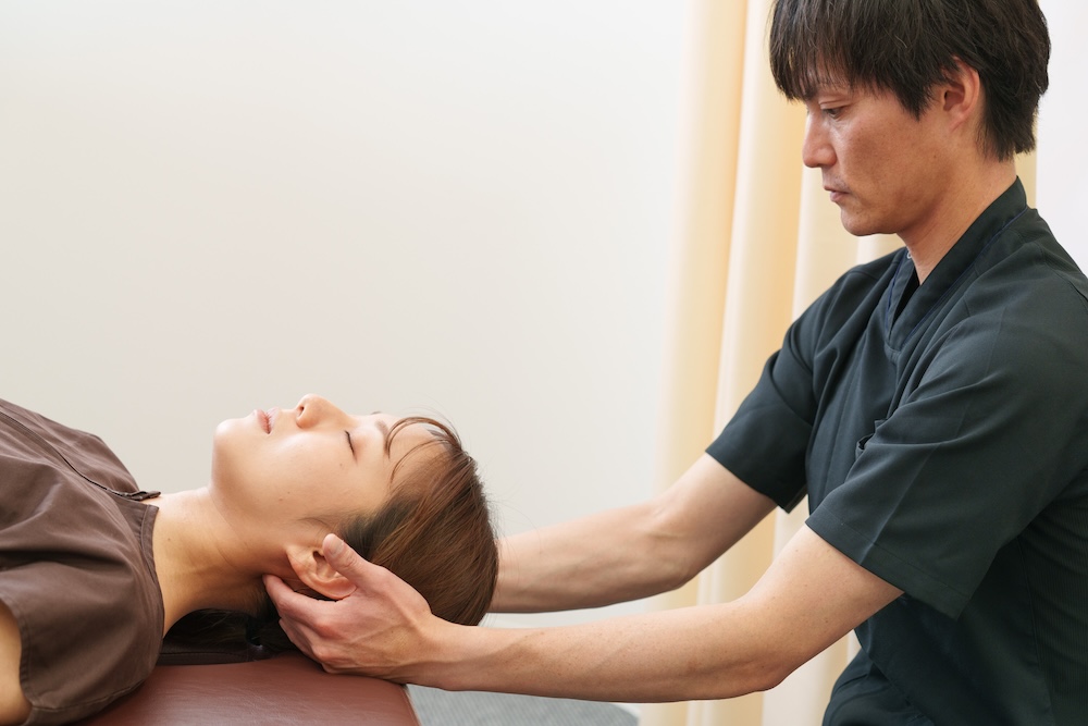 仰向けの患者の首を支えて動かす施術者