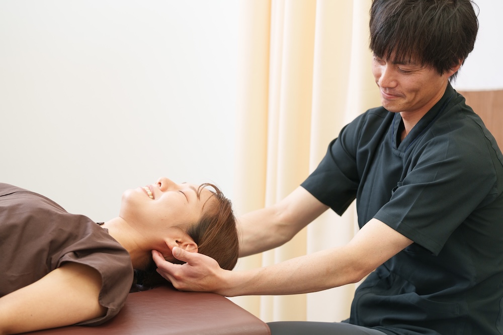 仰向けの患者の頭や首を整える施術者