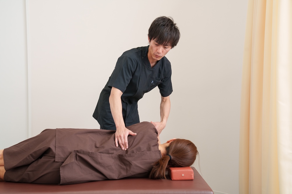 横になった患者の肩甲骨周囲を施術する施術者