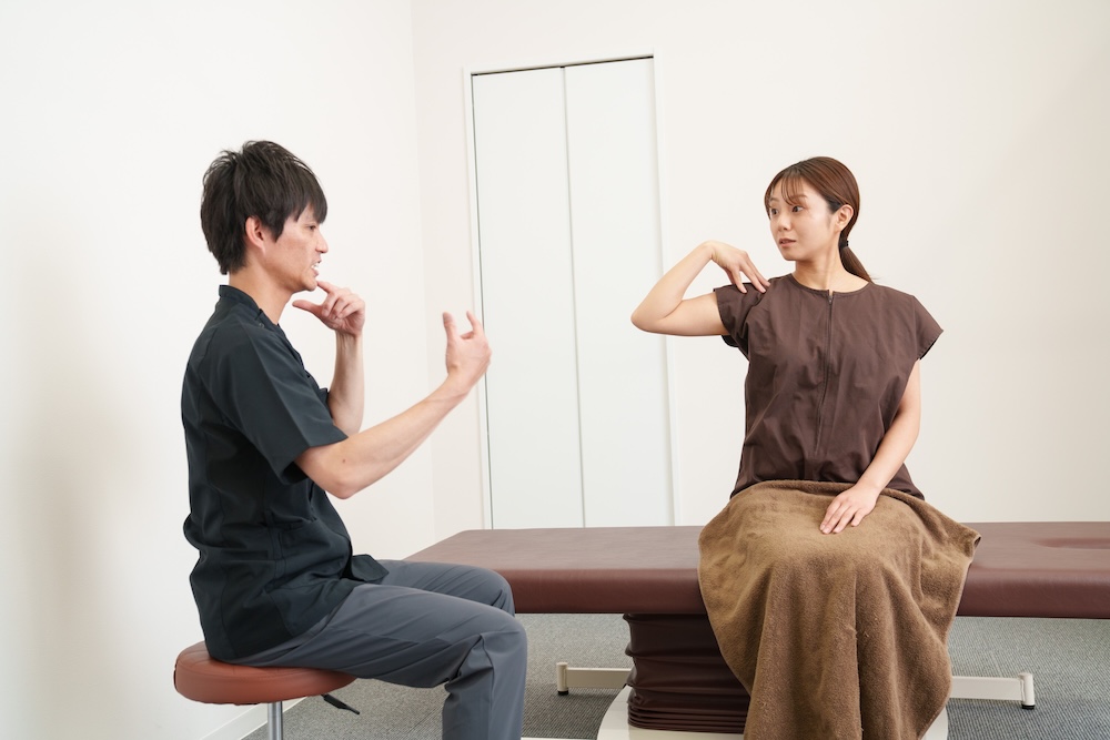 立位で姿勢やセルフケアを伝える施術者と患者