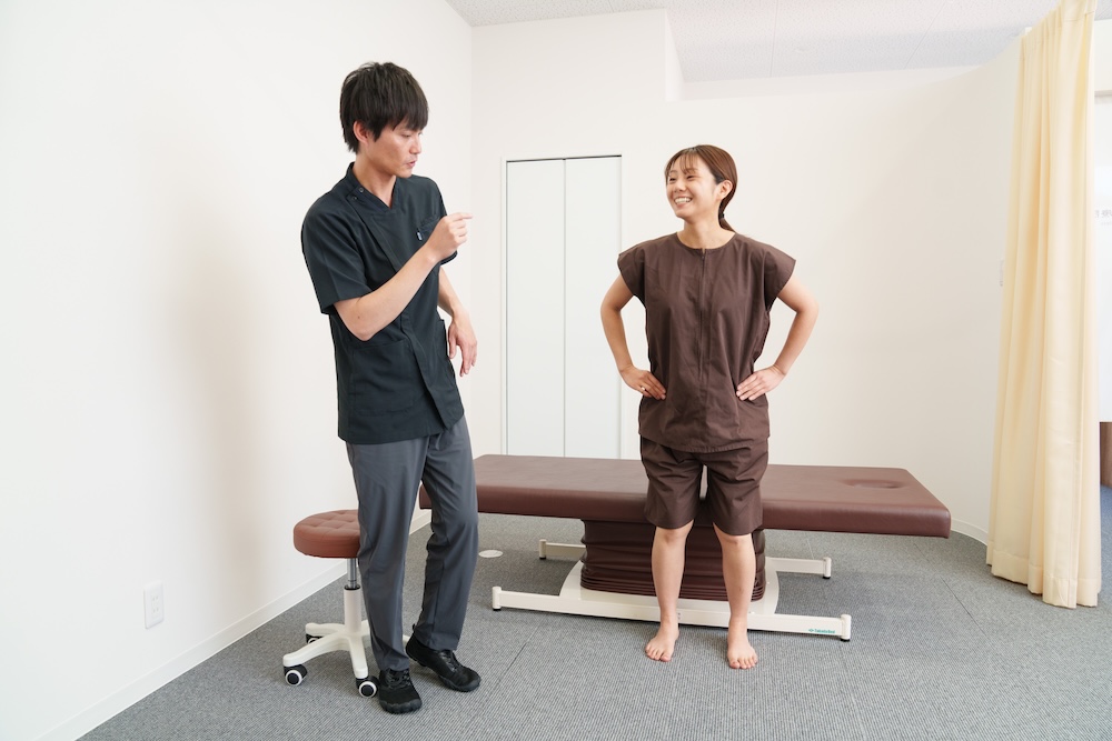 立位でセルフケアの姿勢を伝える施術者と患者