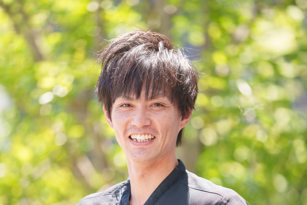 新緑を背に微笑む施術者の上半身